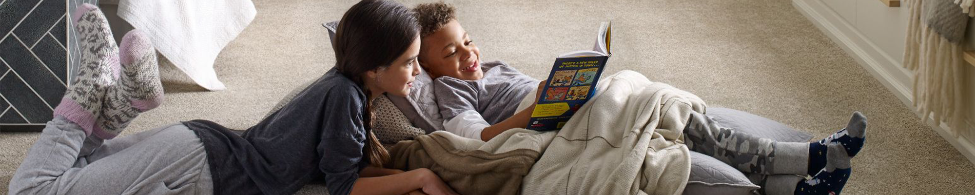 two kids laying on carpet in bedroom reading a book